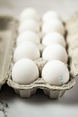 Ten white eggs in a cardboad package on a marble table
