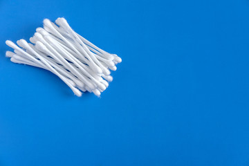 White cotton buds, collected in a pile, lie at the top left on a blue background.