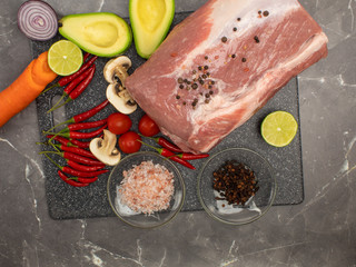 Raw pork meat on a marble board with spices and vegetables top view