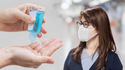 young Asian woman wearing surgical face mask versus hand using wash hand sanitizer gel dispenser...