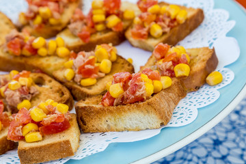 Tasty savory tomato Italian appetizers, bruschetta, toasted bread garnished with garlic, corn, basil, olive oil