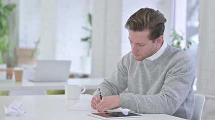 Young Man Writing on Paper at Work