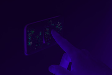 Ultraviolet UV blacklight exposing germs and virus on hand touching dirty light switch