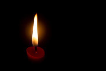 Red candle with yellow flame on black background