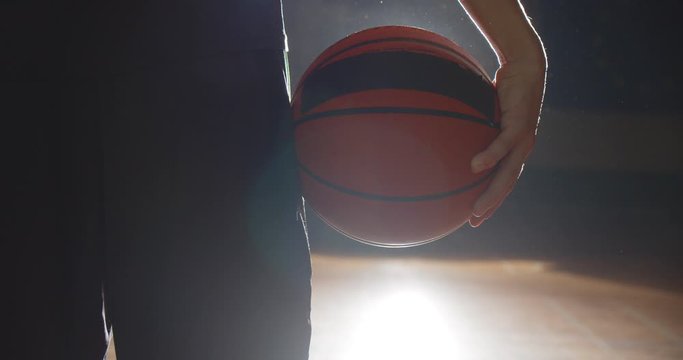 Close-up of a basketball player holding a ball bright light shadow silhouette
