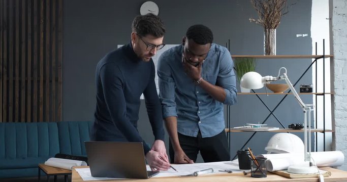 In Busy Engineering Bureau Two young Engineers Discussing Technical Issues over Blueprints. Their Loft Office Looks Minimalistic and Modern. Shot in Slow Motion. Architects. Engineers. Designers.