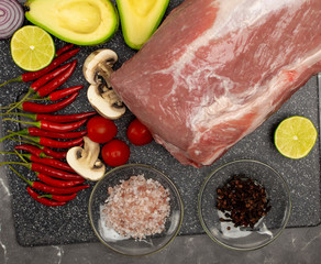 Raw pork meat on a marble board with spices and vegetables