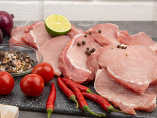Raw pork steaks on a marble board with spices and vegetables