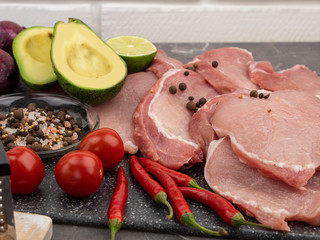 Raw pork steaks on a marble board with spices and vegetables