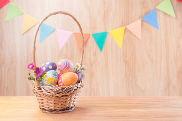 Happy Easter day colorful eggs and flowers in the basket and rabbit on wooden floor have blurred celebrate banner party flags with copy space