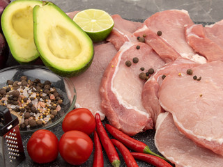 Raw pork steaks on a marble board with spices and vegetables