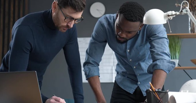 Two professional Architects go over blueprints in industrial Office, discussing. Experienced Creative Designer and Engineer Works with Afro-American Architect in Loft Office. Engineering. Architects.