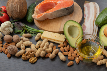 Keto foods on wooden background: meat, fish, avocado, cheese, vegetables, nuts.  Ketogenic low carbs ingredients for healthy weight loss diet, top view, copy space.  Clean eating, healthy fats