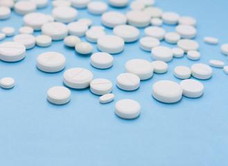 Heap of white pills, tablets, capsules on blue background. Drug prescription for treatment medication health care concept wth copy space.