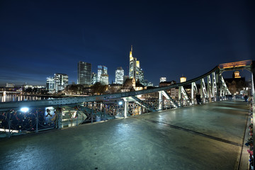 Obraz premium Der eiserne Steg in Frankfurt mit den Hochhäuser in der Nacht