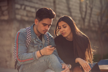 Portrait of young couple sit on a park bench and look at photos on a smartphone