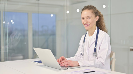 Cheerful Young Female Doctor Working on Laptop in Office