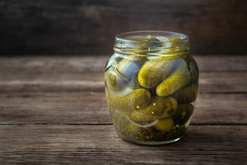 Pickled cucumbers in a glass jar on a wooden background. Copy space for text.