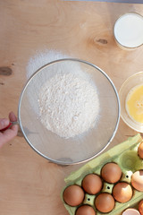 Hands break a raw egg. Stir the protein with the yolk. Sifting flour through a sieve on a wooden background. Glass bowl with mix of egg.