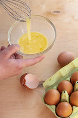 Hands break a raw egg. Stir the protein with the yolk. Glass bowl on a wooden background and a whisk. Cooking.