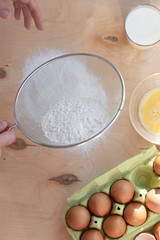 Hands break a raw egg. Stir the protein with the yolk. Sifting flour through a sieve on a wooden background. Glass bowl with mix of egg.