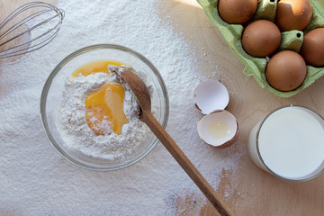 Cooking dough. A raw egg. Stir the protein with the yolk. Sifting flour through a sieve on a wooden background. Glass bowl with mix, towel and wooden spoon.