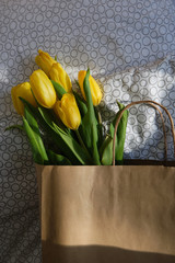 Bouquet of yellow tulips in a paper bag. Beautiful spring fresh flowers in the sun. Floral romantic mood. Nice gift for woman. Springtime blossom, tulips bunch. Women’s holiday celebration