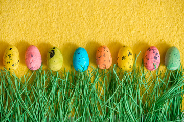 Fototapeta na wymiar Easter concept with colorful eggs on a fluffy yellow background, green grass.