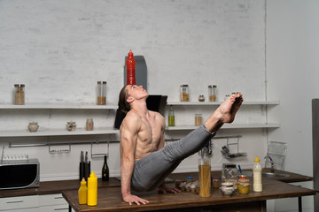 Creative photo of muscular man in the kitchen balancing bottle with souse 