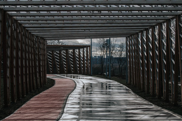 Bicycle and jogging paths passing under wooden decorations in the form of a tunnel in cloudy weather without people.