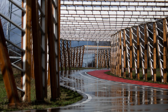 Bicycle and jogging paths passing under wooden decorations in the form of a tunnel in cloudy weather without people.