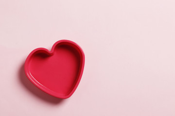 Colorful silicone cooking utensils in the shape of a heart on a pink background