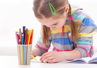 Adorable young female pupil carefully working in her copybook, on white background