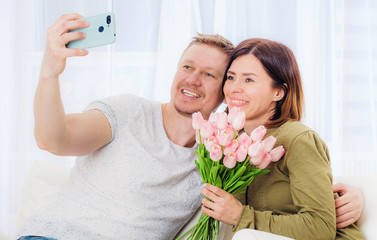 Family couple taking selfie with flower bouquet on cellphone