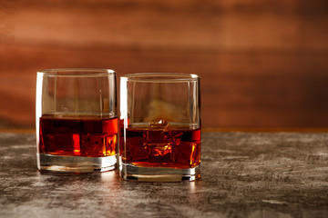 Whiskey with ice or brandy in a glass on a rustic background. Whiskey with ice in a glass. Whiskey or brandy. Selective focus.