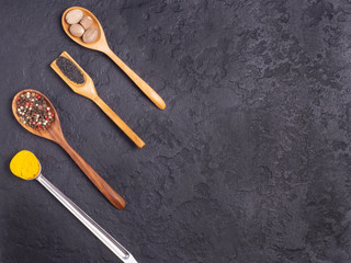 Fototapeta na wymiar Different spices in wooden and metal spoons on a black concrete background.