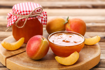Apricot jam in bowl and jar on brown wooden table