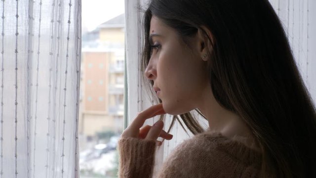 Sad woman thinking looking outside the window feeling lonely