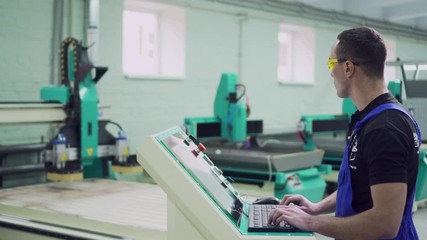 A young male operator of a CNC machine stands at the control panel in the workshop. Slider shot.