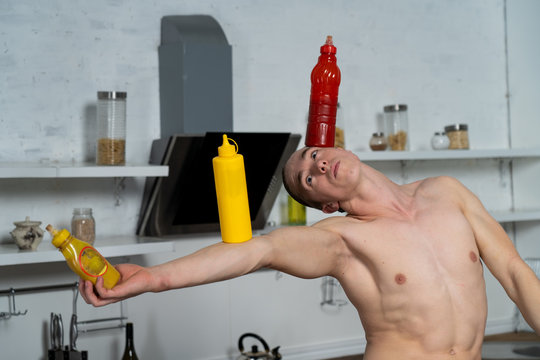 Creative Photo Of Muscular Man In The Kitchen Balancing Bottle With Souse 