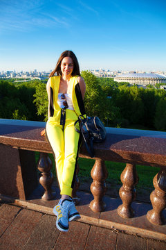 Happy woman in a yellow jumpsuit sits on the railing against the backdrop of the Sparrow Hills in Moscow