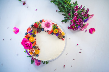 Sweet white cheesecake torte with fresh fruits and rose flowers for celebration on white wooden table