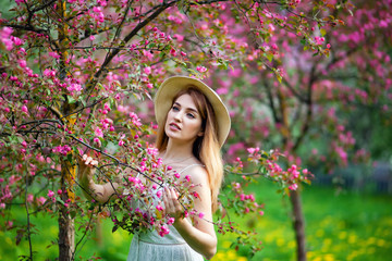 Beautiful teen redhead girl enjoying life in spring blossoming garden against blooming trees. Young dreamy thoughtful lady in nature at sunset. Springtime at countryside concept