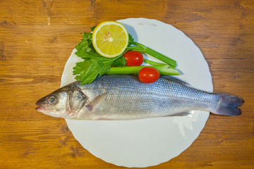 Dish with sea bass, lemon, celery and tomatoes on wooden background. Concept: cuisine based on fish