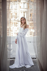 Fashion beauty bride in a long white dress on the terrace against the backdrop of the city. The perfect look for a modern bride.