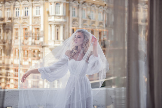 Modern bride on the background of the old city in a long veil. A veil covers the face of a beautiful bride. A modern and light wedding image of the bride.