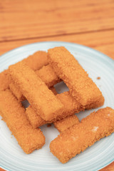 Fried fish sticks on the plate above wooden background
