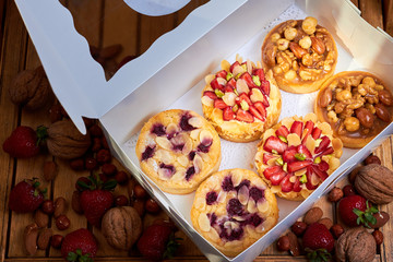 White paper box with six mini tart cupcakes. Tarts with with strawberries, nuts and blueberries. Top view