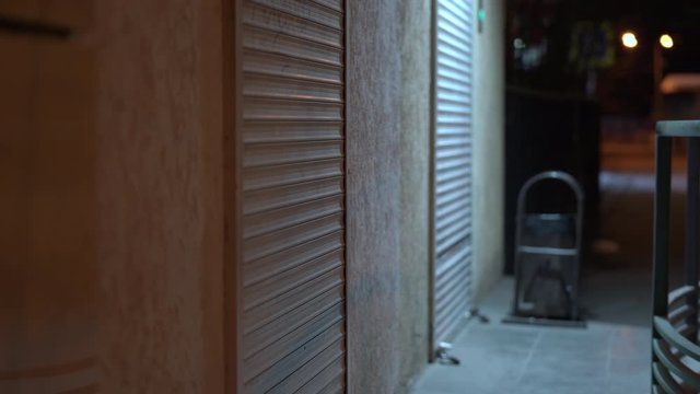 Empty night city street, roller shutters at closed shop door.