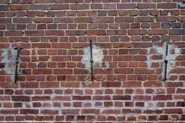 mur extérieur en brique rouge avec des renforts métalliques soutenant des poutres.